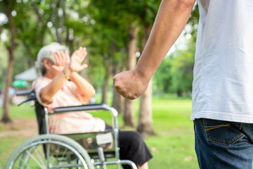 elderly woman in wheelchair covering face and man with fist